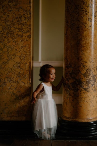 Smiling child in white dress by marble column.
