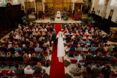 Bride walks down church aisle with guests seated.