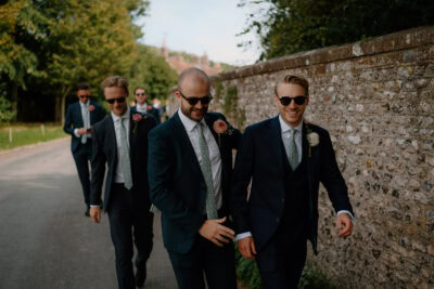 Groomsmen in suits and sunglasses walking on road