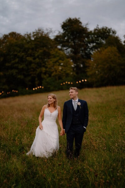 Wedding couple walking in a grassy field.