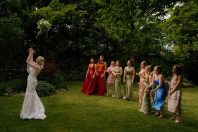 Bride throws bouquet to bridesmaids in garden.
