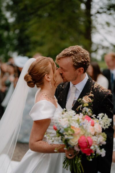 Wedding couple kissing surrounded by guests and flowers.