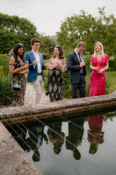 Group of people enjoying drinks by garden pond.