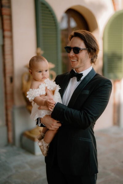 Man in suit holding baby in white dress.
