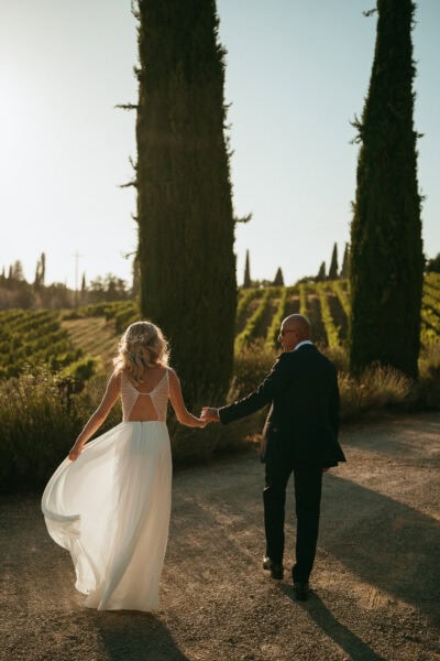 Couple walking hand in hand through vineyard.