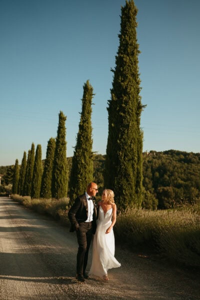 Couple walking on tree-lined path at sunset.
