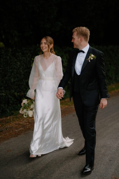 Bride and groom walking hand in hand outdoors.