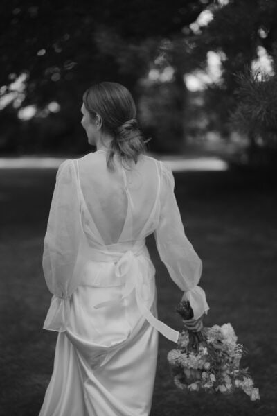 Woman in wedding dress holding flowers, outdoor setting.