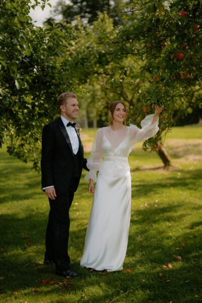 Bride and groom under an apple tree in orchard.