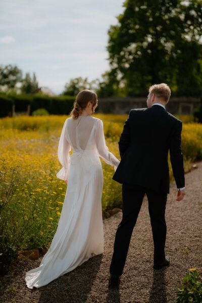 Couple walking in sunny garden, wedding attire.