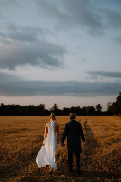 Couple walking through golden field at sunset.