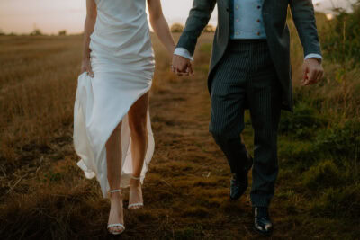 Couple walking hand-in-hand in field at sunset.