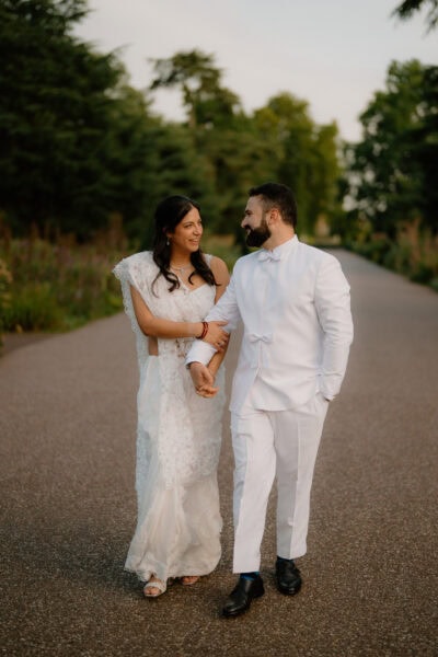 Couple walking in park, dressed in wedding attire.