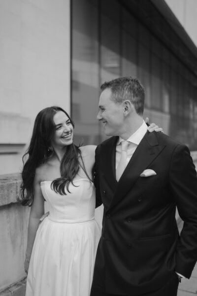 Smiling couple in wedding attire embracing outside.