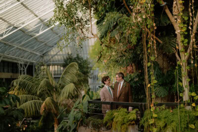 Couple in greenhouse surrounded by lush greenery.