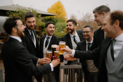 Groomsmen celebrating with pints outdoors.