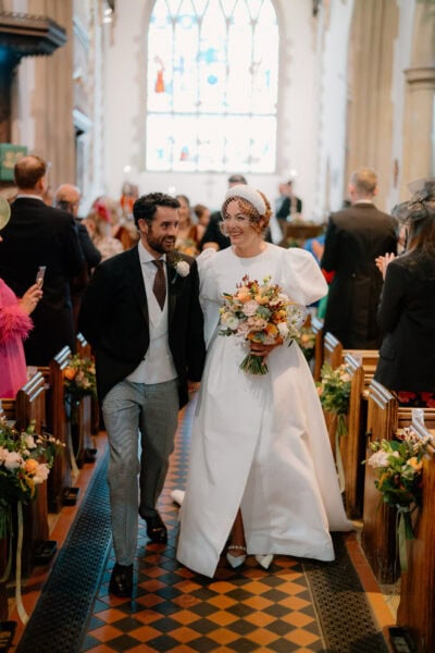 Bride and groom walking down church aisle, smiling.