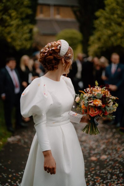 Bride in white dress holding bouquet outdoors.