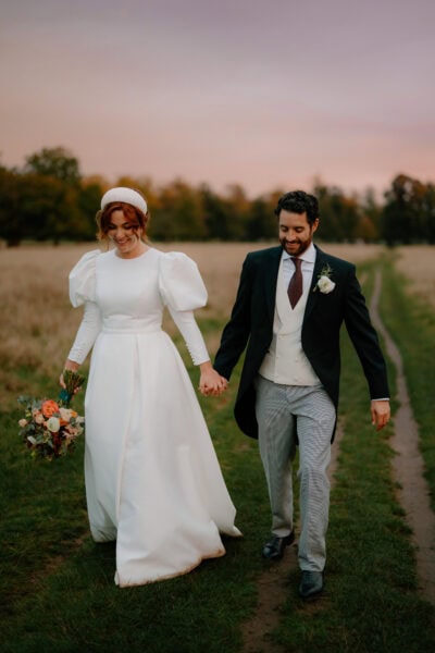 Bride and groom walking in field at sunset.