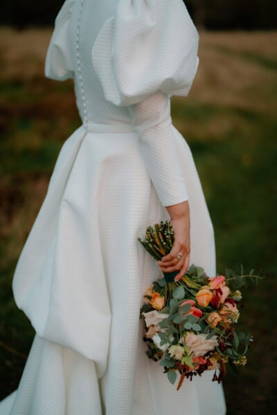 Bride holding colourful bouquet, wearing textured dress.