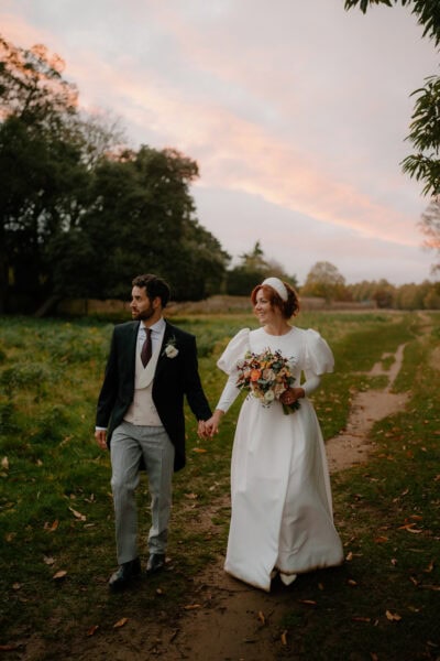 Bride and groom walking in countryside at sunset.
