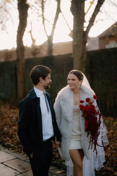 Couple walking, dressed in wedding attire, autumn setting.