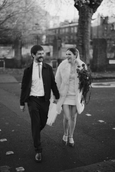 Couple walking outdoors, smiling on wedding day.